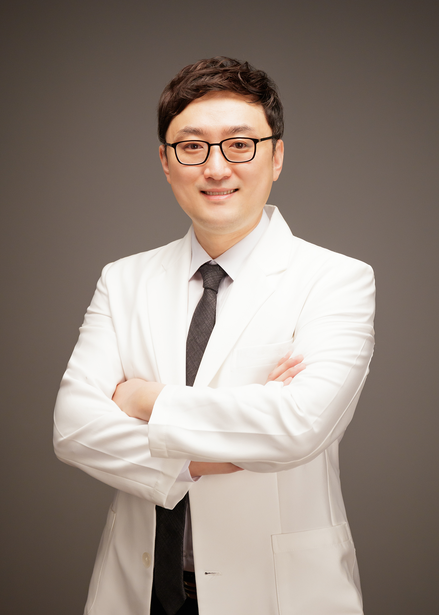 안경을 쓰고 흰 진료 가운을 입은 남성 원장이 팔짱을 끼고 정면을 바라보는 스튜디오 인물 사진